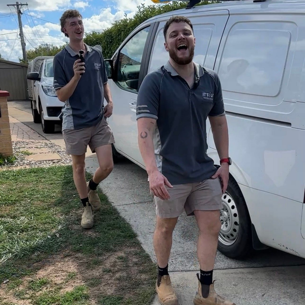Two smiling people walking beside a white van on a sunny sidewalk.
