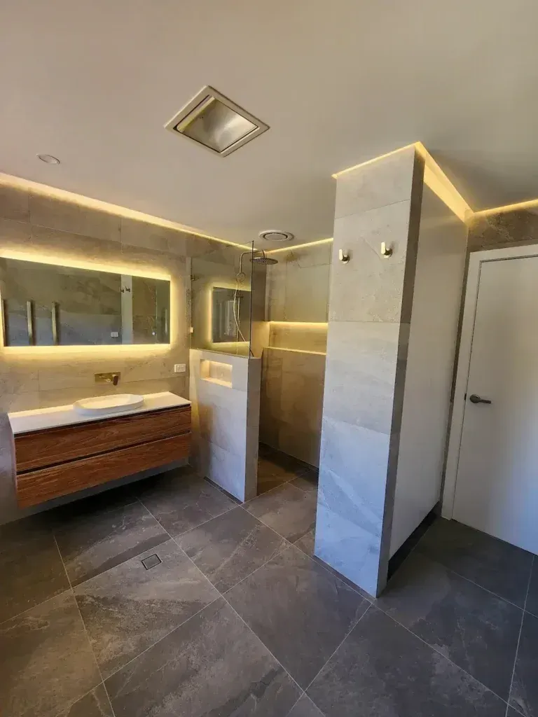 Modern bathroom with wood vanity, gray tile, and lit accents.