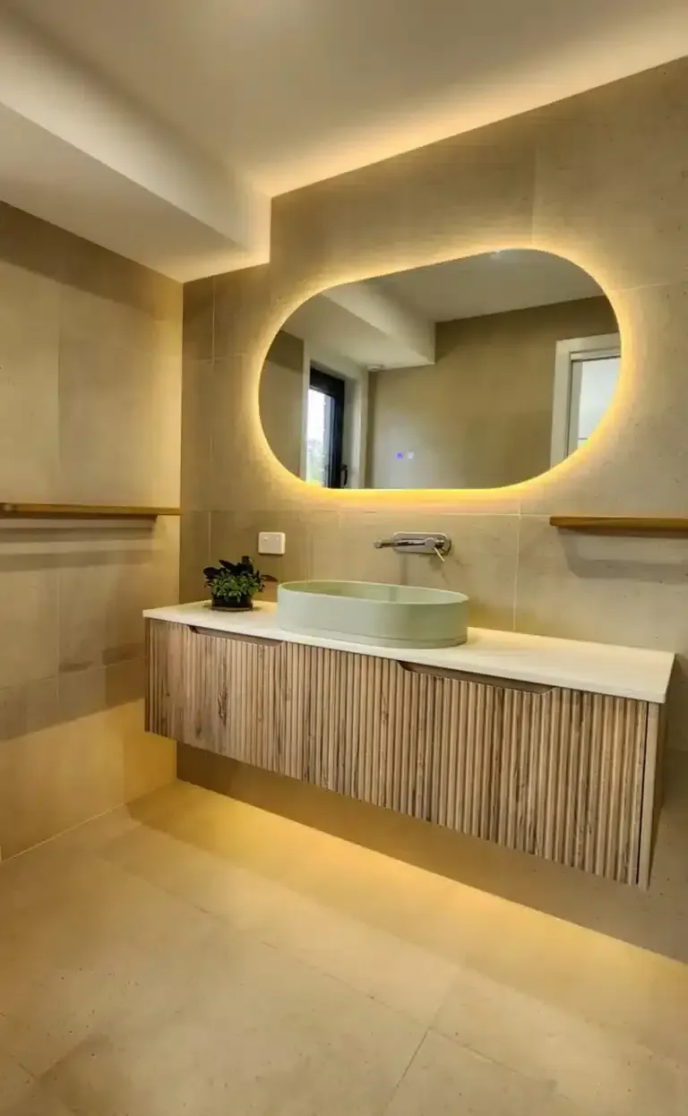 Modern bathroom with illuminated oval mirror, floating wooden vanity, and a light green sink.