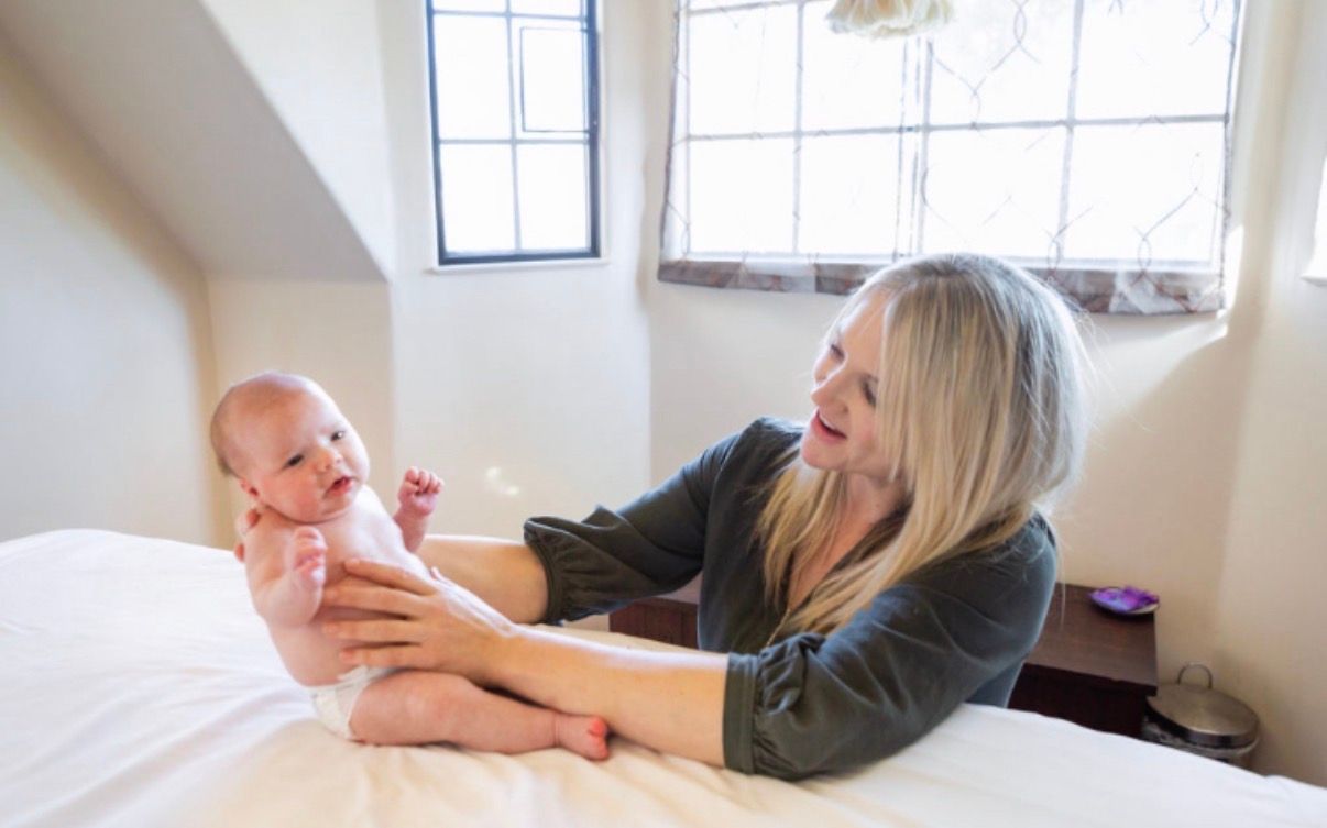 Woman holding a baby on a bed near a bright window