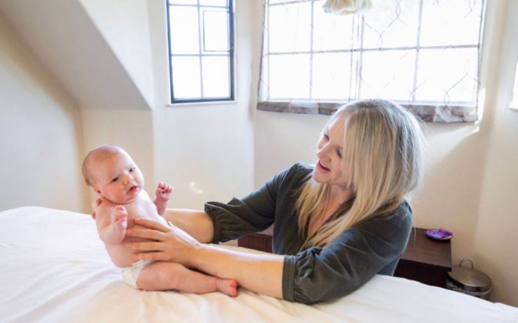 Woman holding a baby on a bed near a bright window