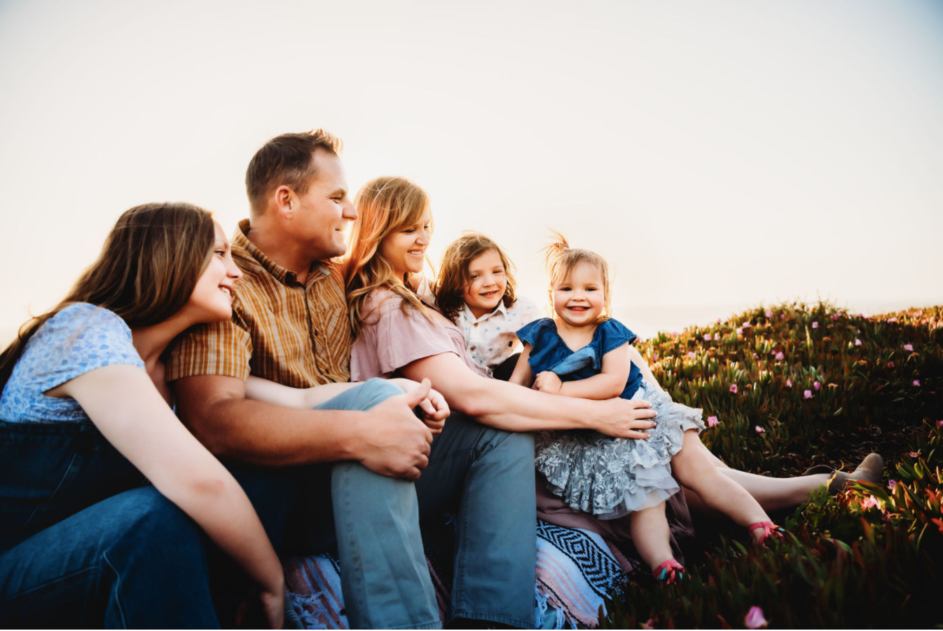 Family sitting together on a couch outdoors at sunset, smiling and hugging in a garden.