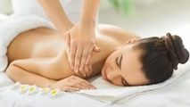 Person receiving a shoulder massage while lying face down on a white spa bed, with flowers nearby