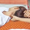 Person lying on orange mat with hands behind head, eyes closed, resting indoors