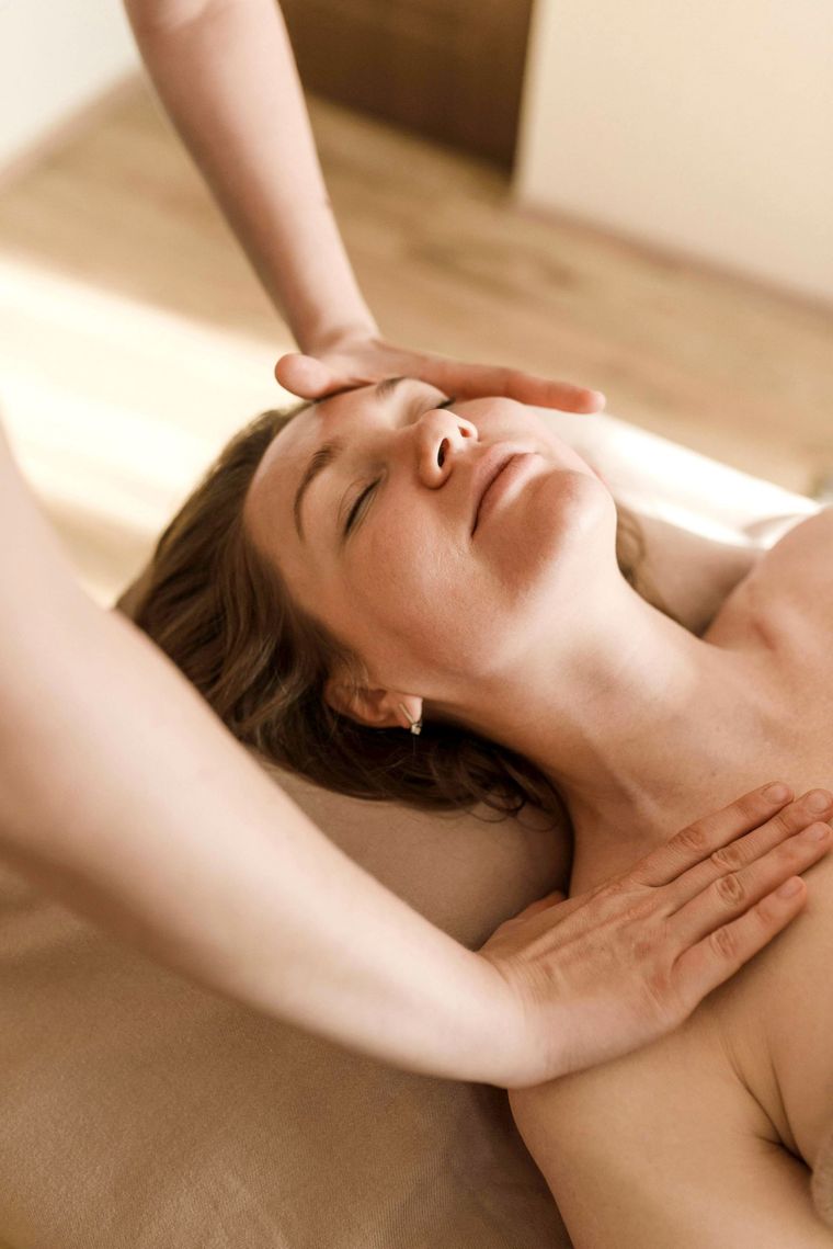 Person receiving a forehead massage while lying on a spa bed, eyes closed in a bright room