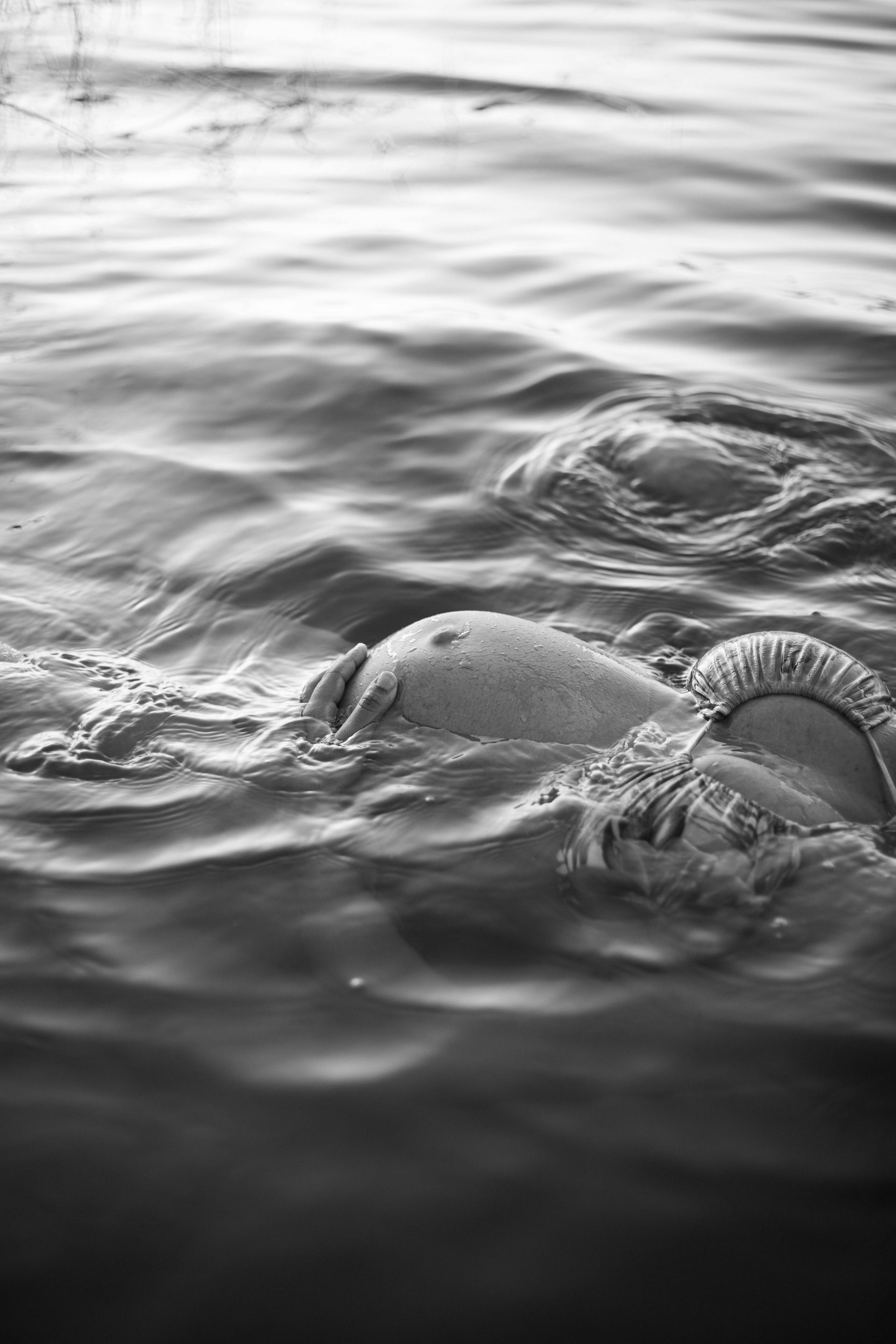 A pregnant woman floating peacefully in choppy water, seen in black and white.