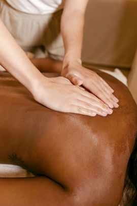 Hands massaging a person’s back with lotion in a warm spa setting