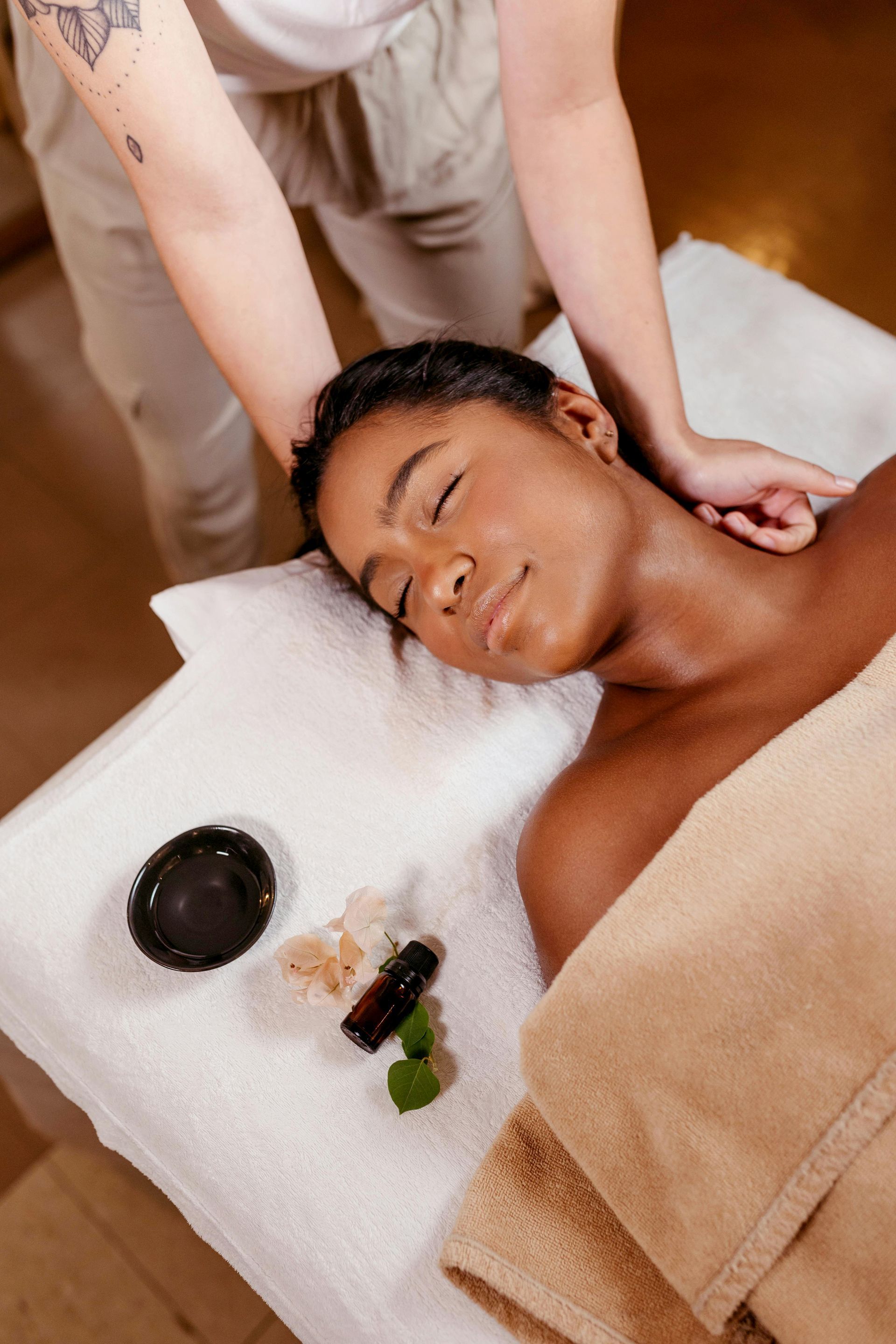 Spa massage with a person receiving a neck massage on a towel, with oils and stones nearby.