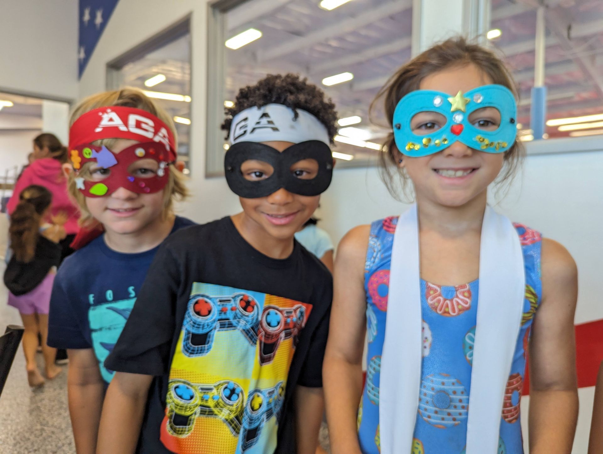 Three children wearing colorful superhero masks and capes standing outside a building