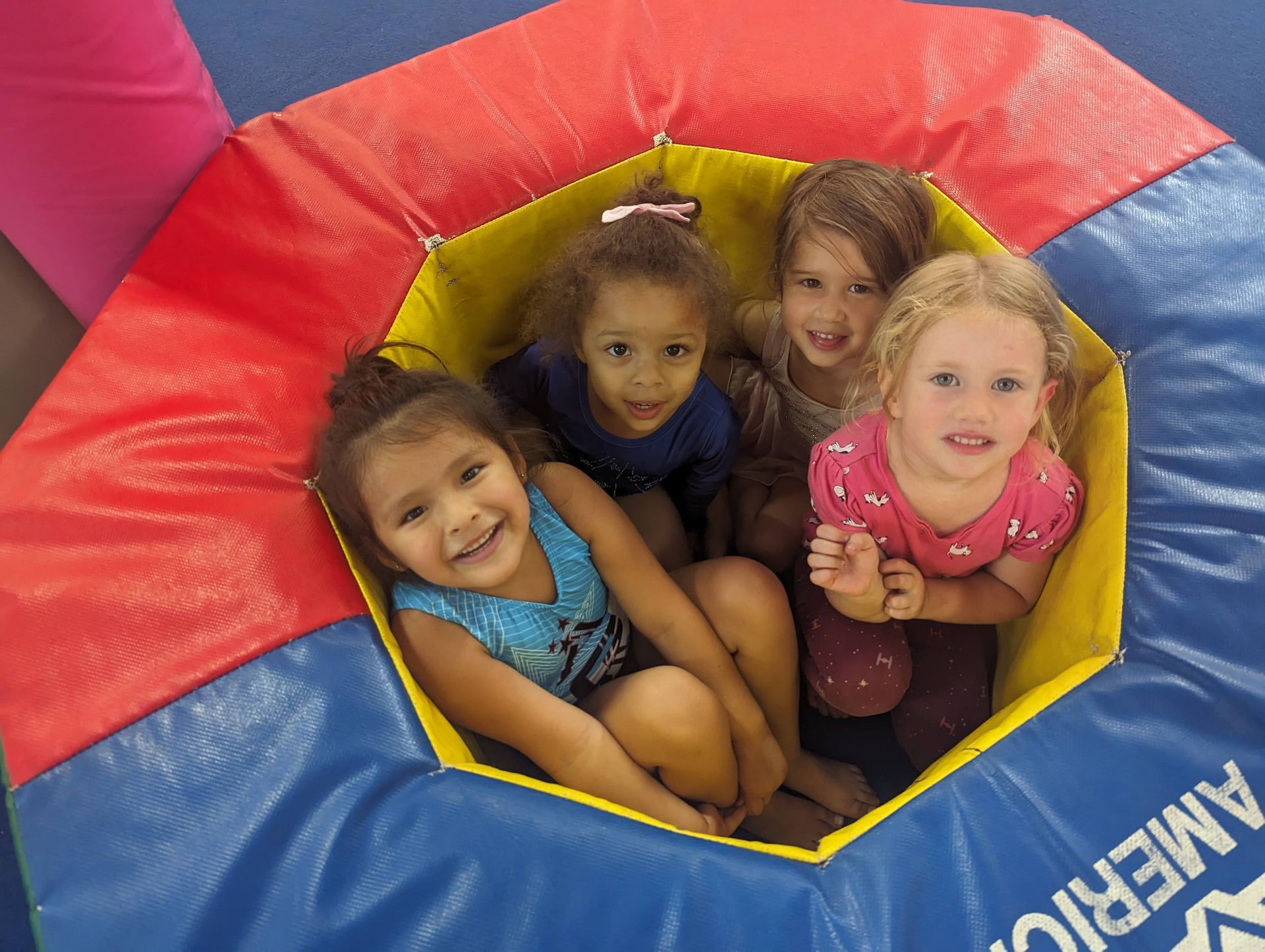 Four children smiling inside a colorful red, yellow, and blue inflatable play tunnel