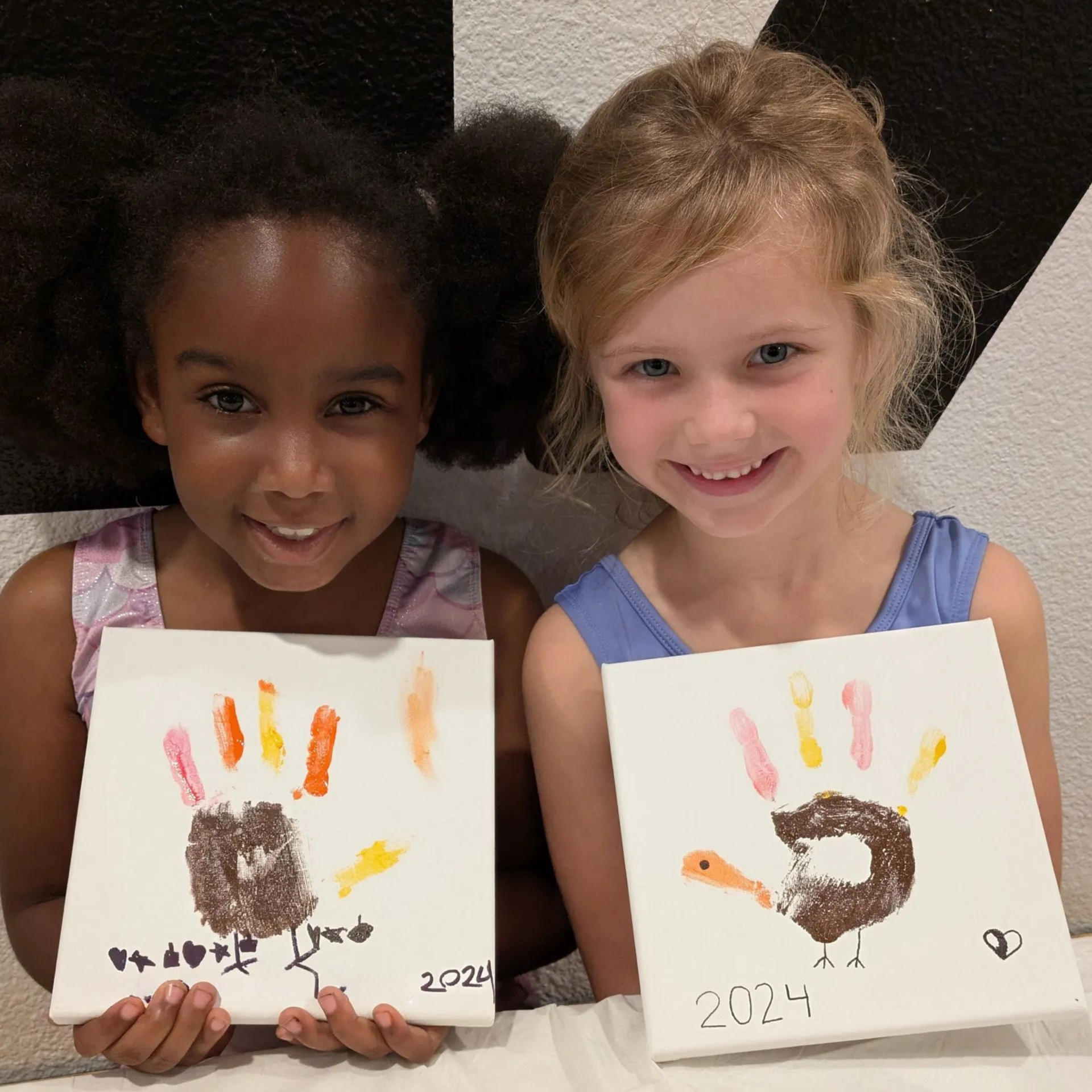 Two children smiling and holding handprint art with colorful paint on paper.