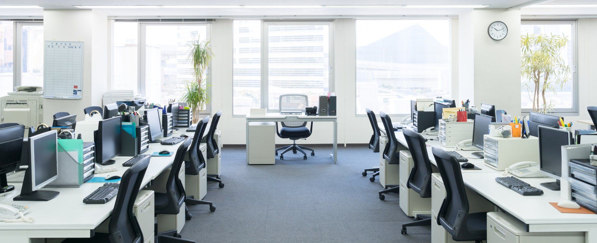 An empty office with lots of desks and chairs and a clock on the wall.