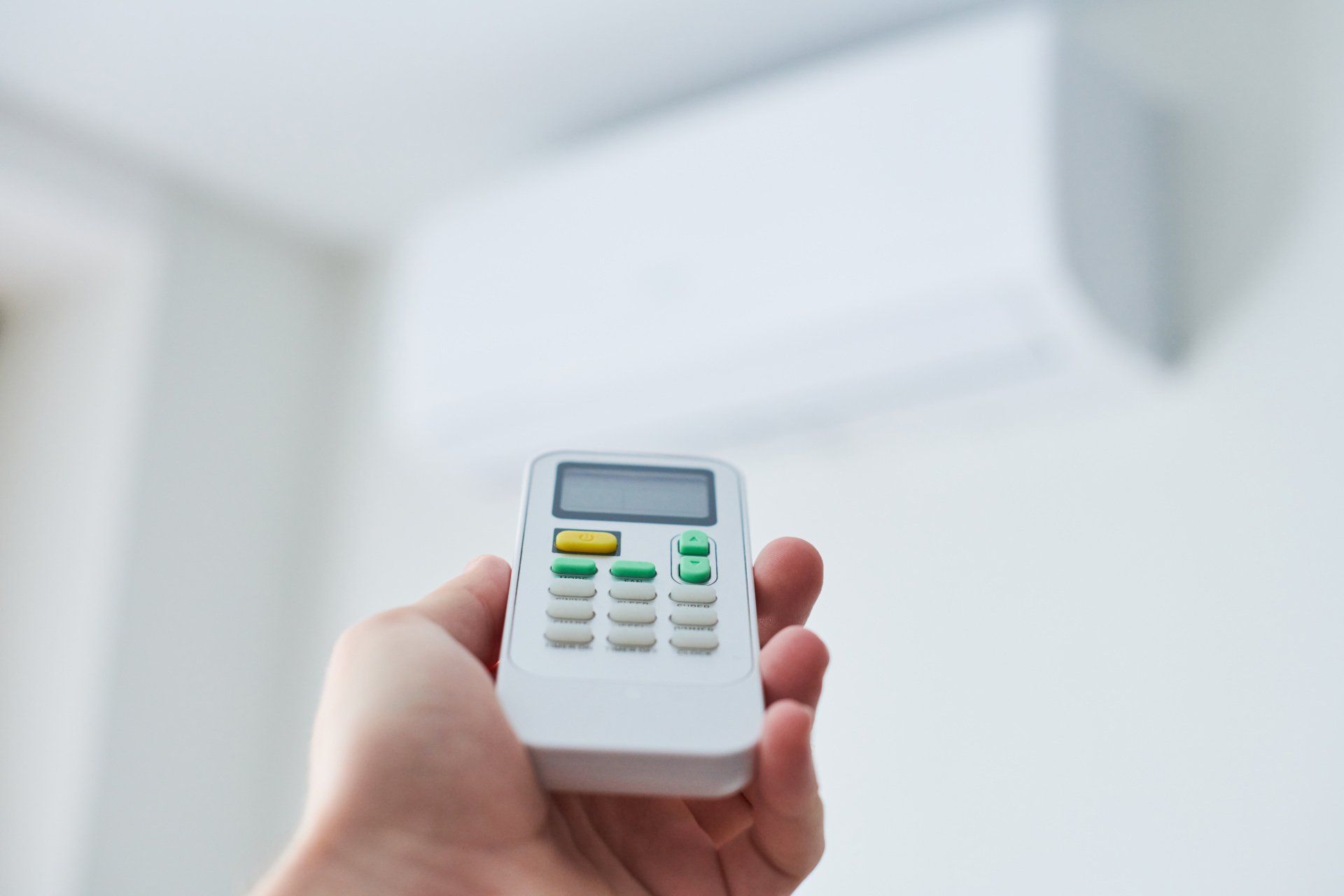A person is holding a remote control in front of an air conditioner.