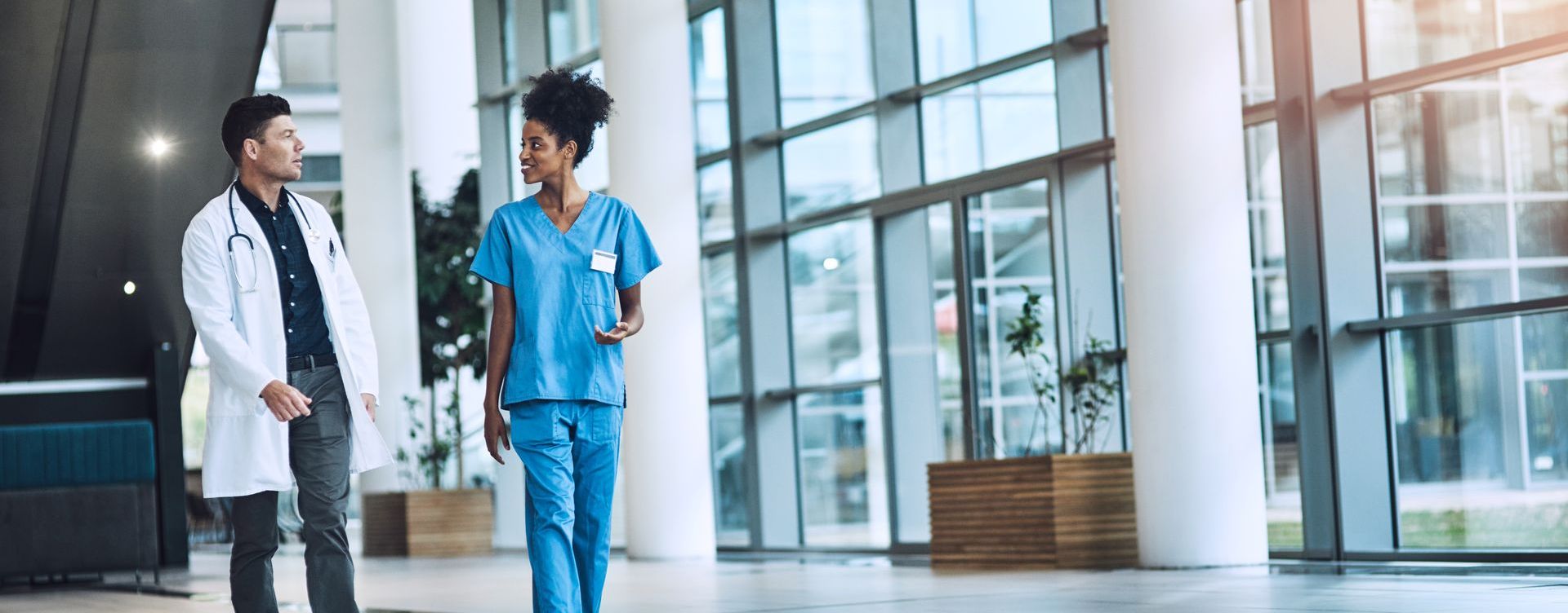 A doctor and a nurse are walking through a hospital lobby.