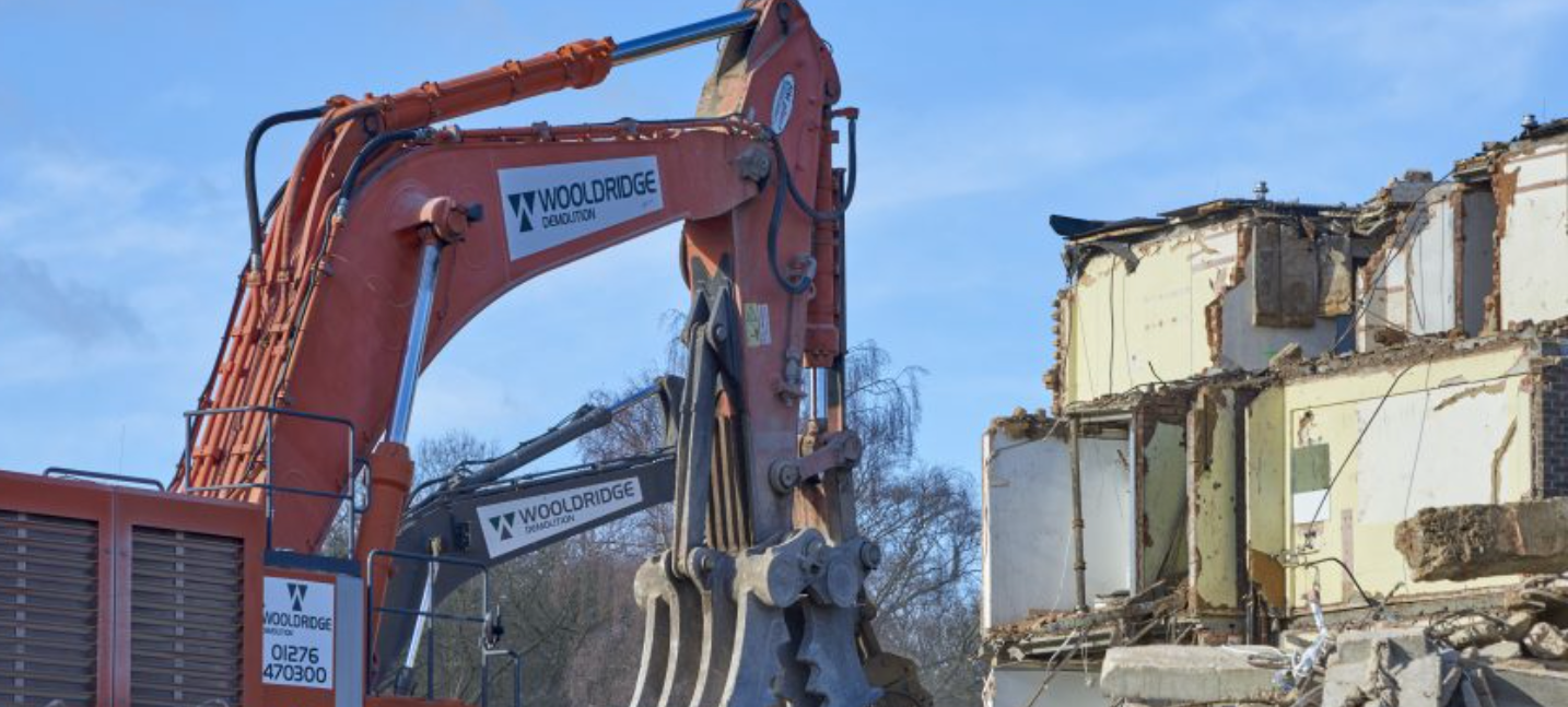 A large orange excavator is demolishing a building.