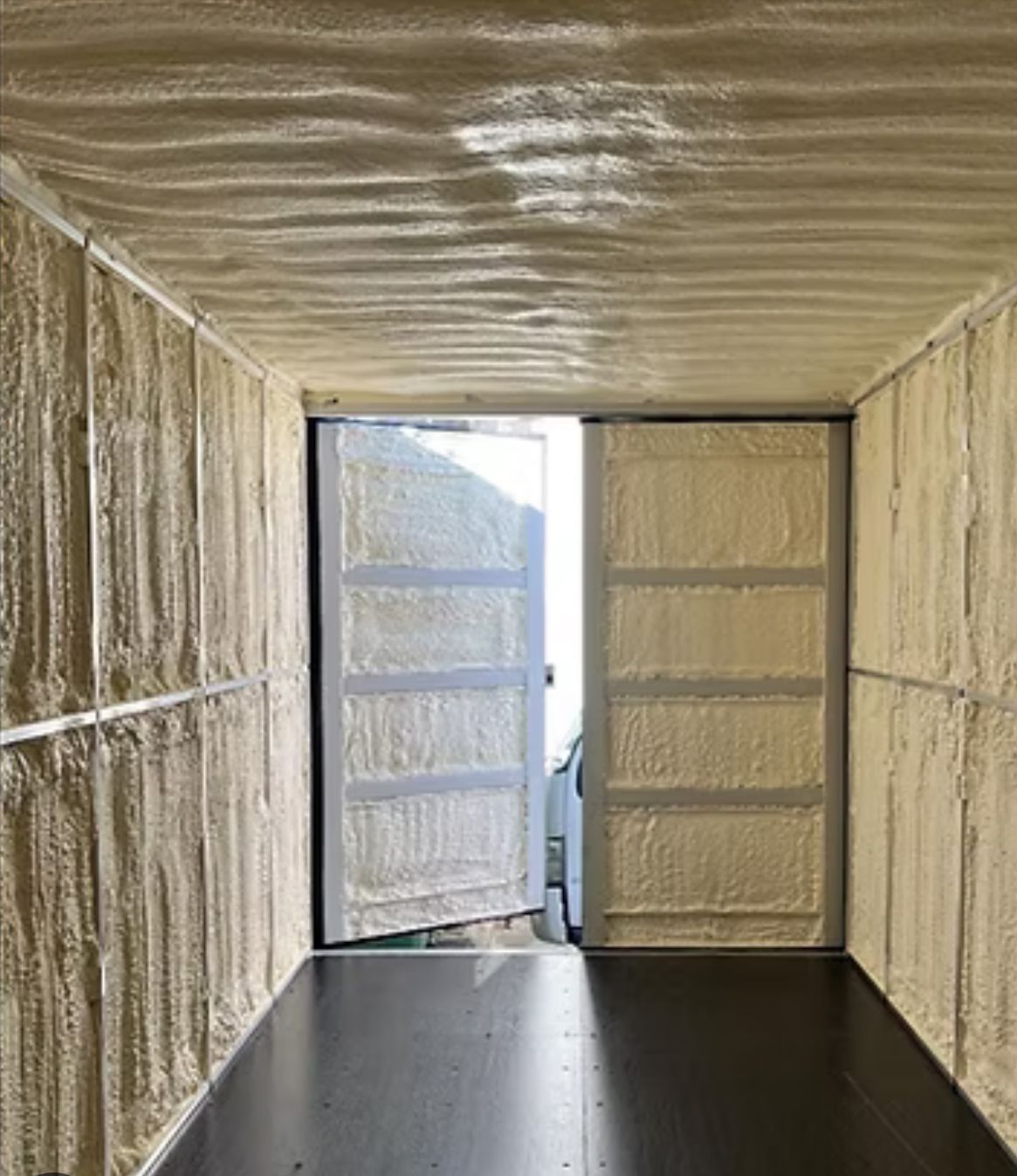 Interior of a shipping container with walls and doors covered in beige spray foam insulation, with open doors — Proshield Insulation & Waterproofing In Shell Cove, NSW