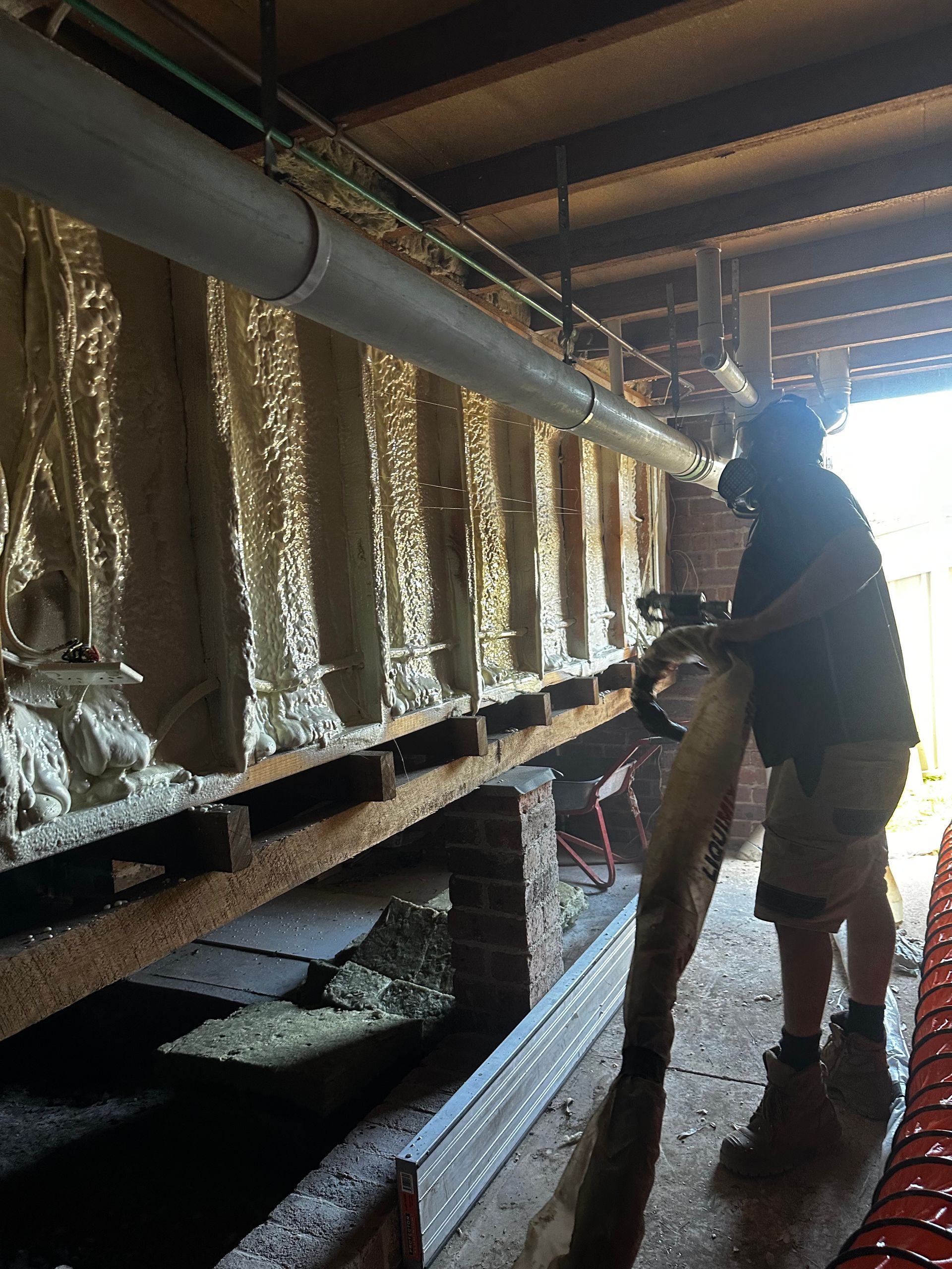 Person spraying foam insulation in crawlspace. Beige foam covers a rectangular structure — Proshield Insulation & Waterproofing In Shell Cove, NSW