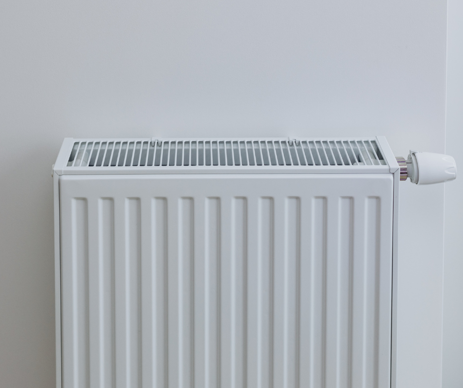 A white, vertical panel radiator mounted on a plain white wall, featuring a dial for temperature control on the right.