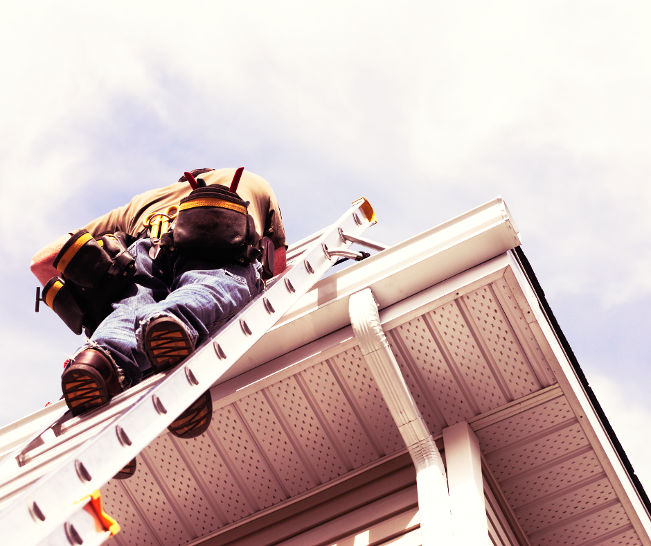 A person in a tool belt climbs a metal ladder leaning against the side of a house to reach the roofline.