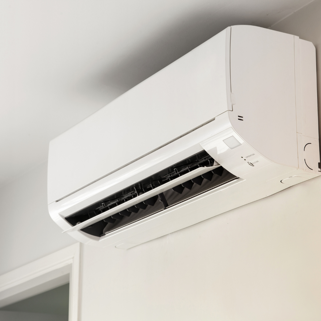 A white wall-mounted air conditioning unit installed high on a white wall.