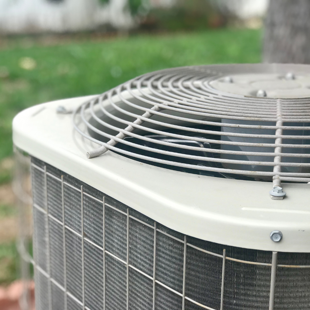 A close-up of a residential outdoor air conditioning unit featuring a beige metal top and a protective metal grate.