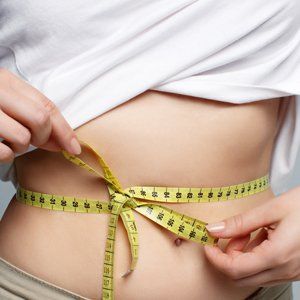 Measuring tape wrapped around a bare waist over white fabric