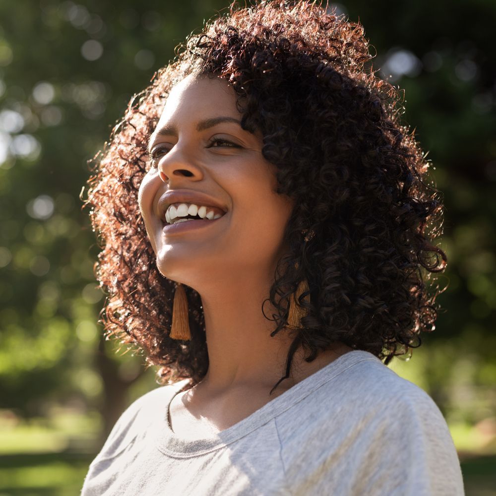 Woman With Small Hip A woman with curly hair is smiling in a park.