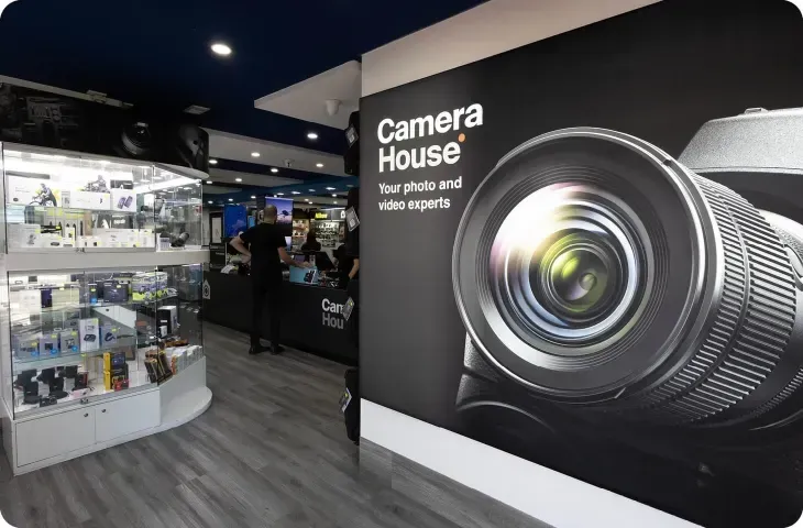 Camera House store interior with camera lens graphic. Displays with products, people behind counter.