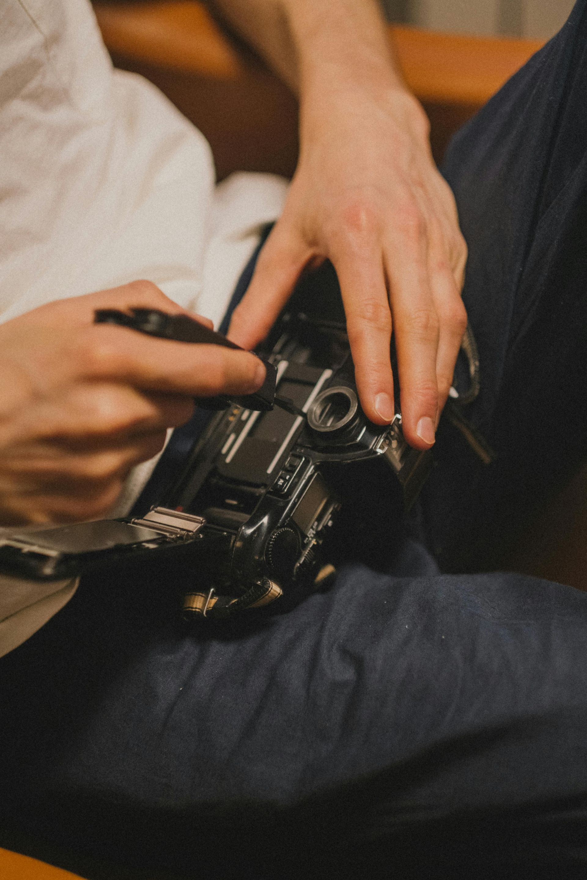 Person adjusting black camera on lap with a tool. Wearing white shirt and blue jeans, seated.