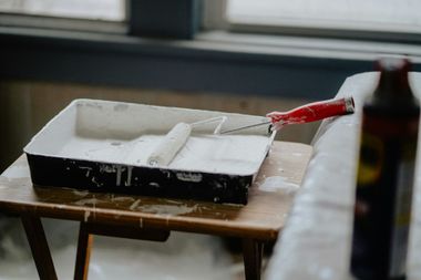 Paint tray with white paint and a red-handled roller on a small table