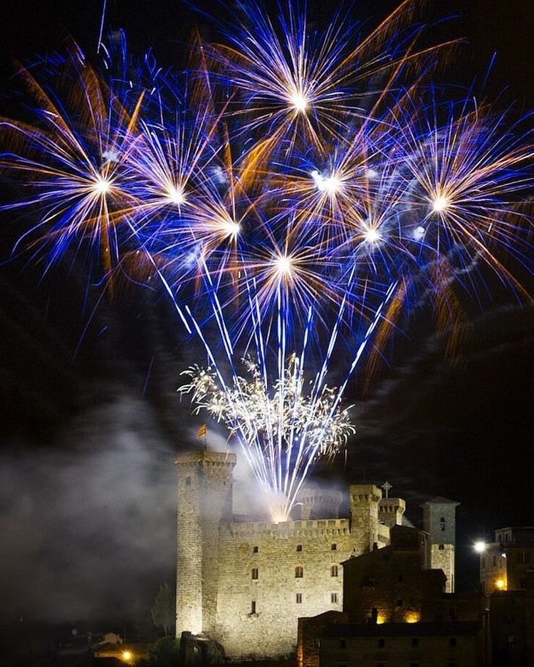 Di notte, fuochi d'artificio esplodono su un castello di pietra; esplosioni blu e arancioni illuminano la scena.