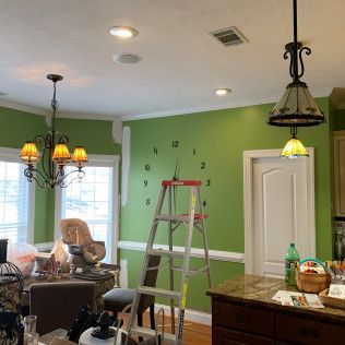 Kitchen under renovation with green wall, ladder, ceiling lights, and wall clock decals