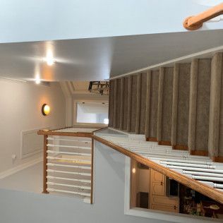 Modern staircase landing with wood railing, gray walls, and a vaulted ceiling in a bright interior.