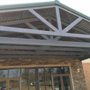 Entrance of a stone building with glass doors and a large covered roof supported by white beams