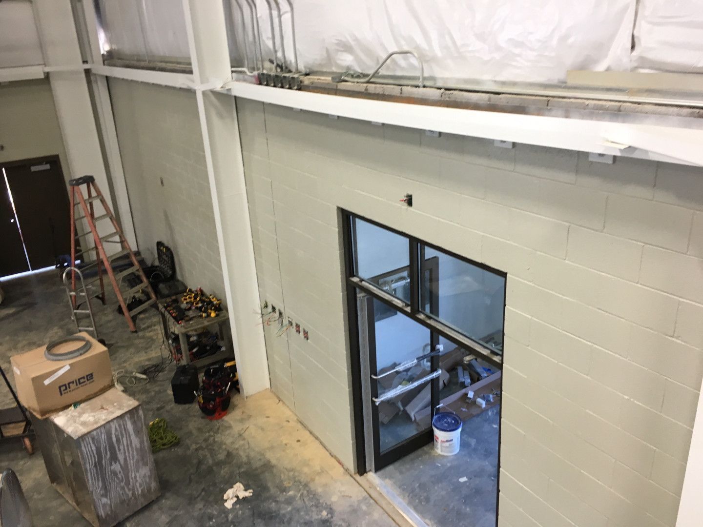 Indoor warehouse loft with white walls, windowed office door, and construction materials below a mezzanine.