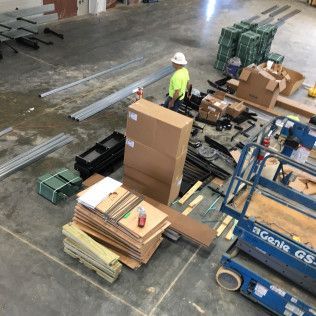 Warehouse worker beside stacked boxes and lumber next to a blue lift in an industrial workspace
