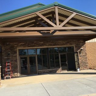 Storefront entrance with glass doors, brick facade, and a red ladder on the left under a green-trimmed awning.