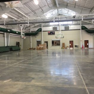 Empty indoor gymnasium with polished concrete floor, green bleachers, and overhead basketball hoops.