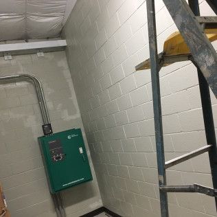 Basement utility room with a green wall-mounted electrical panel and metal ductwork on cinderblock walls