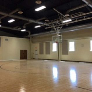 Empty indoor basketball court with wood floor, tan walls, and ceiling lights