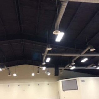 Interior of a large room with a dark ceiling, bright hanging lights, and a light-colored wall with a monitor