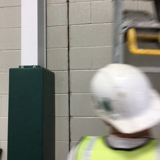 Person in a white hard hat near a green padded post in an indoor gym or facility