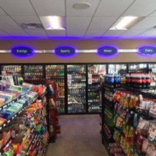 Grocery store aisle with colorful snack shelves and lit signs for energy, sports, water, and dairy.