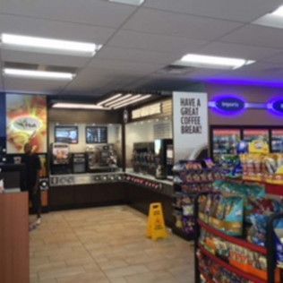 Convenience store coffee area with snack racks, menu screens, and a wet floor sign
