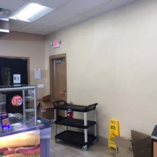 Empty beige room with a doorway, wall cart, and a yellow wet floor sign near a counter area.