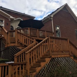Wooden outdoor staircase with railings leading up to a brick house deck under a black umbrella