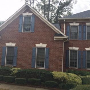Red brick house facade with blue shutters and a manicured hedge in front.