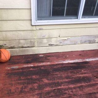 Weathered red deck beneath a house window, with a basketball resting at the left edge