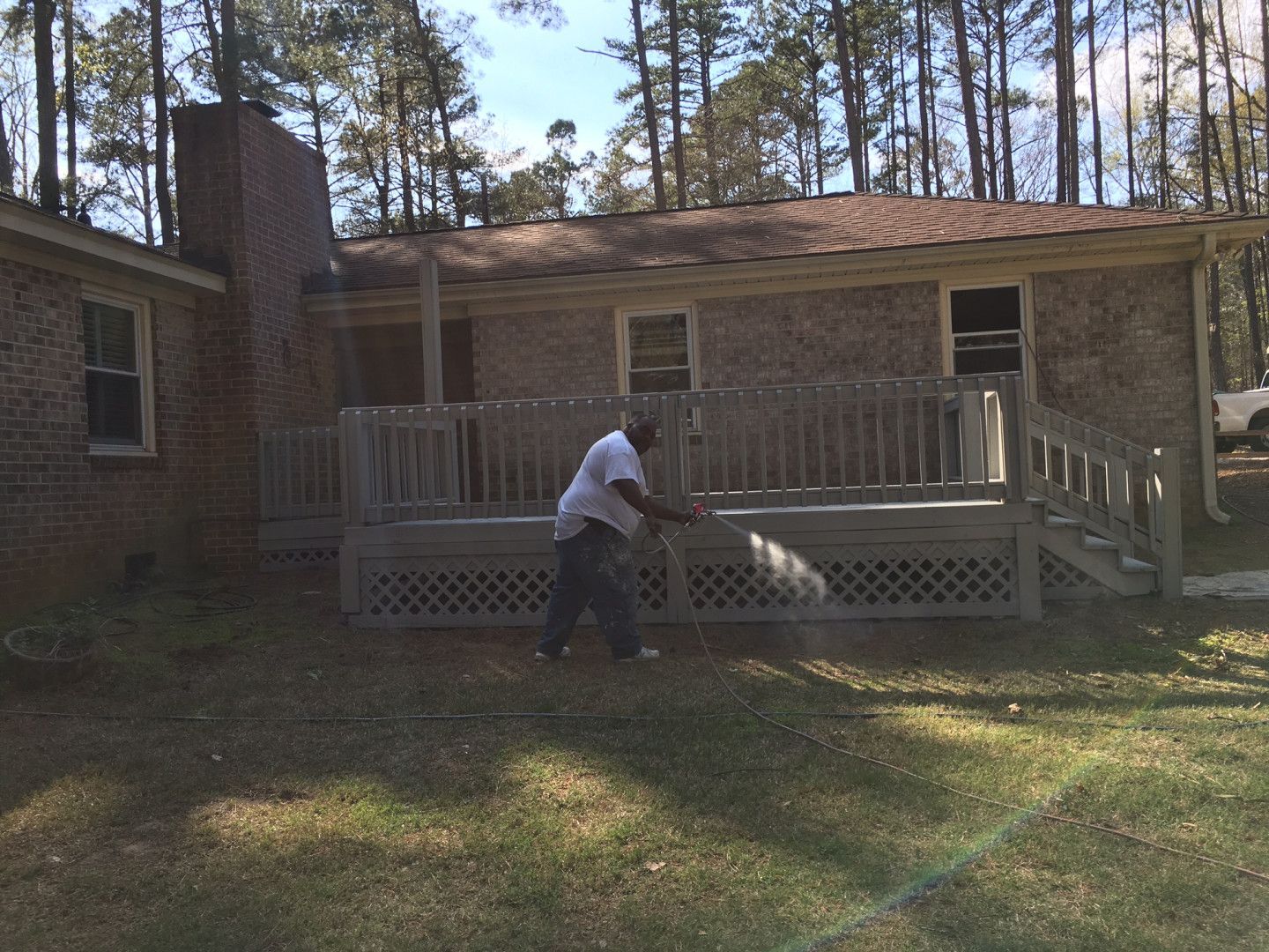 Person washing the front porch of a brick house with a hose on a sunny day