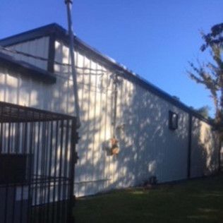 White industrial building with blue trim beside a fenced grassy area under a clear sky